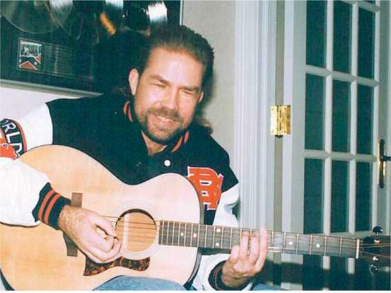 Dated photo of John Jarrard playing an acoustic guitar